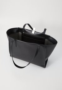 Sac fourre-tout en cuir noir au texture lisse, avec une ouverture en haut et un fermoir en argent. Il dispose d'un grand compartiment principal et d'une poche zippée à l'intérieur.