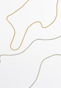 Catene intrecciate in oro e argento posate l'una accanto all'altra, con una texture liscia e uno spessore uniforme in tutto il loro sviluppo.