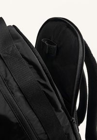 Fekete hátizsák sima, matt felülettel, ívelt zsebbel, cipzáros záródással és strapabíró, állítható pántokkal. Látható tépőzáras rész.