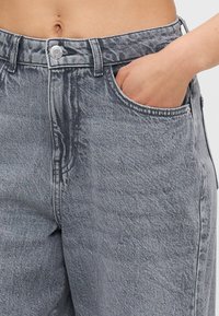 Grå denimjeans med høy midje, teksturert stoff, frontlommer og knappelukking, med et subtilt slitt utseende og kontrasterende sømmer.