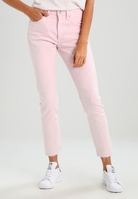 Jeans de mezclilla rosa con un ajuste slim, dobladillo deshilachado y diseño de cinco bolsillos, combinados con zapatillas deportivas blancas.