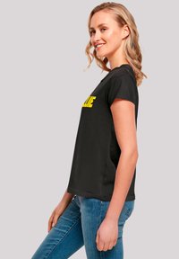 Black cotton T-shirt with short sleeves featuring bold yellow text on the front. Relaxed fit, smooth texture, and crew neckline.