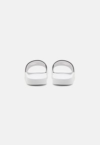Sorte og hvite slip-on sandaler med en gjennomsiktig stropp, flat såle og teksturert overdel. Enkelt design uten utsmykkinger.
