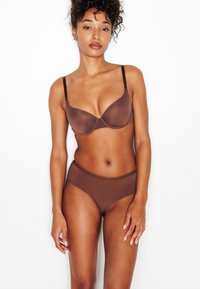 Set di reggiseno e slip in marrone solido, realizzati in tessuto liscio ed elastico. Il reggiseno è dotato di ferretto e spalline regolabili; gli slip hanno una vita alta.