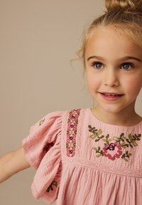 Rotes Baumwollkleid mit floralem Stickmuster in Rot und Grün, gerafften kurzen Ärmeln und Spitzenakzenten am Ausschnitt und Oberkörper.