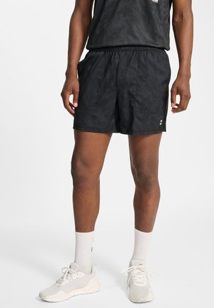 Zwarte sportshorts met een gestructureerd ontwerp, een elastische tailleband en zijzakken. Gecombineerd met lichtgrijze sneakers en witte sokken.
