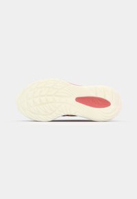 Semelle de chaussure de sport avec une bande de roulement blanche texturée et une zone de grip ovale rouge, présentée sur un fond gris clair uni.