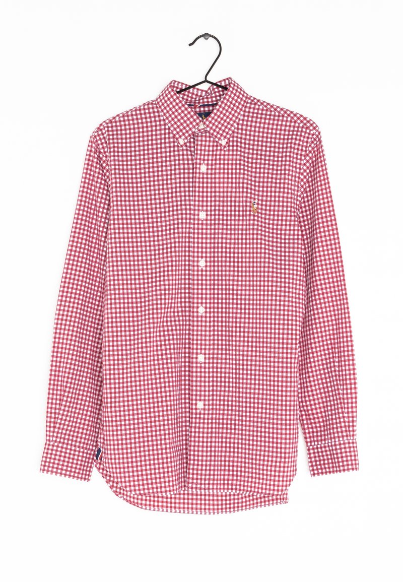 Chemise à manches longues à carreaux rouges et blancs avec col, suspendue sur un cintre noir contre un fond blanc.