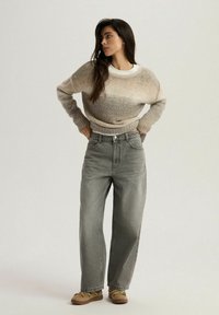 Beżowy sweter dzianinowy z okrągłym dekoltem, zestawiony z szarymi dżinsami o wysokim stanie i beżowymi trampkami. Miękka faktura i luźny krój.