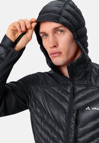 Giacca a puffo nera con cappuccio, caratterizzata da un design trapuntato, chiusura con zip e dettagli con logo. Il tessuto ha una superficie liscia e brillante.