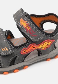 Halleli hallid sandaalid oranžide aktsentide, Velcro-riba, leegikujunduse ja tekstureeritud tallaga, mis tagab haakumise. Hingav materjal ja ergonoomiline kuju.