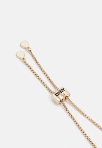Collana d'oro con design a catena, dotata di un pendente cilindrico centrale inciso con "DKNY" e accentuato da un piccolo gioiello.