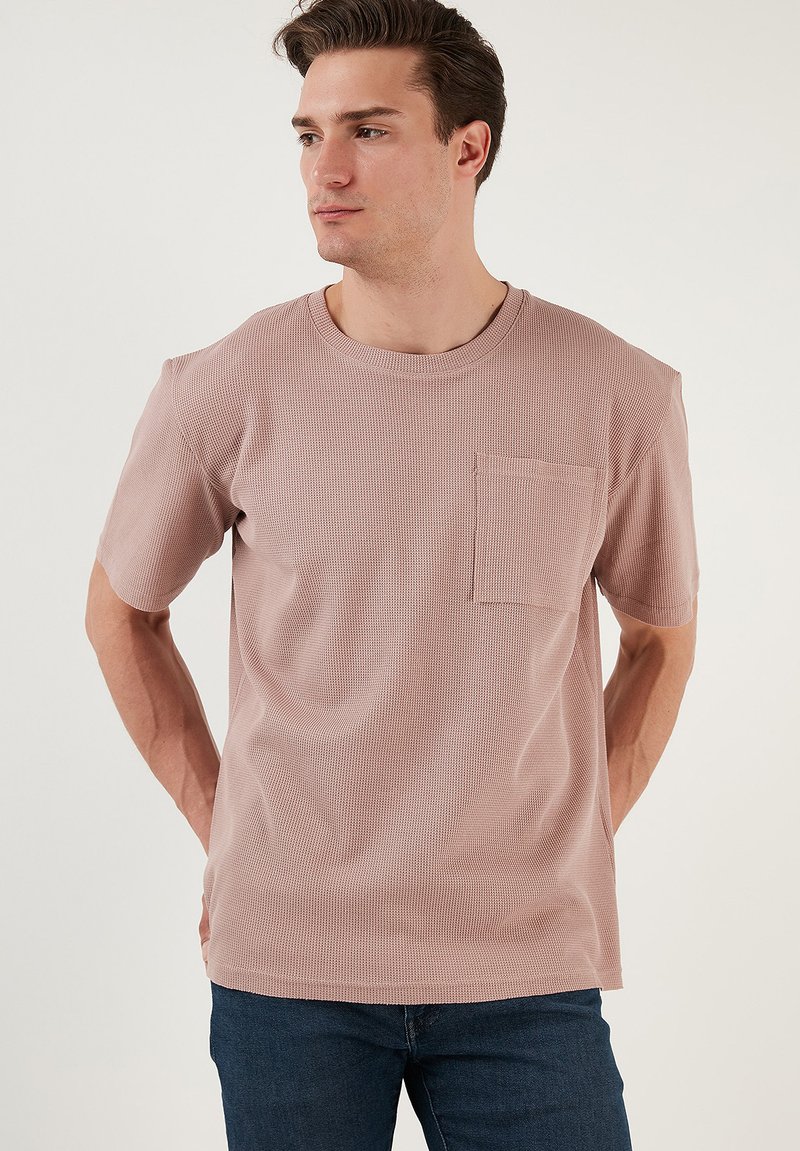 Světle růžové ribbed tričko s kulatým výstřihem a krátkým rukávem, se záševkem na hrudi a volnějším střihem.