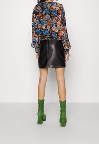 Mini-jupe en cuir noir avec surpiqûres visibles ; blouse imprimée à fleurs avec manches longues ; bottines vertes en daim avec talons carrés.