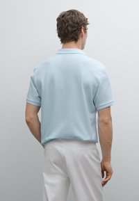 Light blue short-sleeve polo shirt in soft cotton blend with a classic collar, paired with white trousers, showcasing a clean, modern design.
