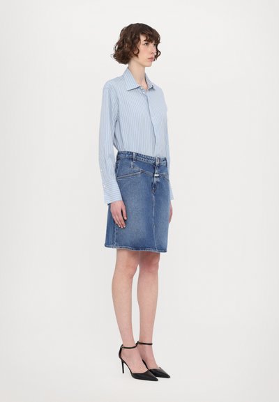 Cămașă din bumbac cu dungi verticale albastre deschise, asortată cu o fustă mini din denim. Outfitul include tocuri negre ascuțite și o siluetă ajustată.