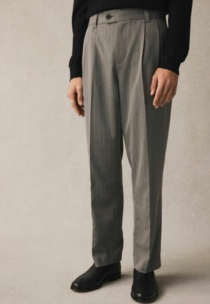 Graue, gefaltete Hose mit vertikalen Streifen, taillierte Passform und glatter Textur. Kombiniert mit schwarzen Lederschuhen, die einen eleganten Look zeigen.