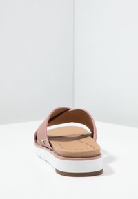 Pink slide sandal with two wide straps, cushioned tan footbed, and white outsole with brown accent. Smooth material, minimalist design.