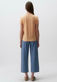 Camicia di cotone color pesco a maniche corte abbinata a pantaloni in denim a gamba larga di un blu chiaro, caratterizzati da una vestibilità rilassata e dettagli di cucitura sottili.