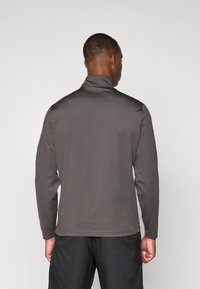 Mørkegrå langærmet pullover med høj hals, glat tekstur og uden synlige mønstre. Stylet med sorte bukser, bagfra vist.