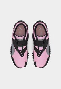 Ροζ και μαύρα αθλητικά παπούτσια Puma με γκρι λεπτομέρειες, ύφασμα από δίχτυ και ελαστικούς ιμάντες που διασταυρώνονται, φωτογραφημένα από πάνω σε λευκό φόντο.