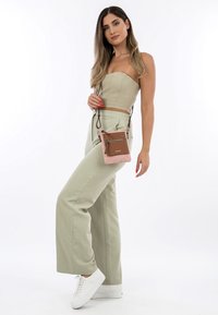Top senza maniche verde chiaro e pantaloni a gamba larga coordinati, abbinati a una piccola borsa a tracolla bicolore rosa e marrone, indossati con sneakers bianche.