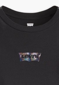 Fekete póló, ribbelt nyakkivágással, melyen a mellrészen holografikus Levi's logó található. Sima textúrájú és testhezálló kialakítású.