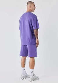 Paarse katoenen t-shirt en short set, met een losse pasvorm en korte mouwen. Afgemaakt met witte sokken en lichtgrijze sneakers.