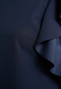 Donker marineblauwe stof met fijne textuur en een zachte, vloeiende ruches langs de rechterrand.