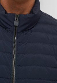 Marineblauwe donzen jas met horizontale doorgestikte banen, hoge kraag en volledige ritssluiting. Het materiaal lijkt glad en lichtgewicht.