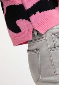 Lyserød strikket sweater med store sorte mønstre og ribbede manchetter. Kombineret med lysegrå denimjeans med almindelige lommer og syninger.