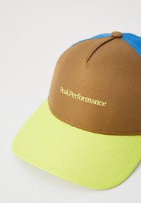 Brun og blå kasket med flad skygge, har neongul underside og "PeakPerformance" logo i gul på frontpanelet.