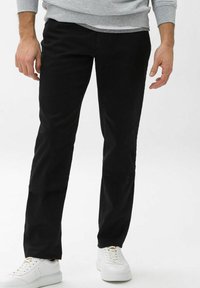 Schwarze Baumwollhose mit geradem Bein, die eine glatte Textur aufweist und mit weißen Sneakers getragen wird. Keine sichtbaren Muster oder Verzierungen.