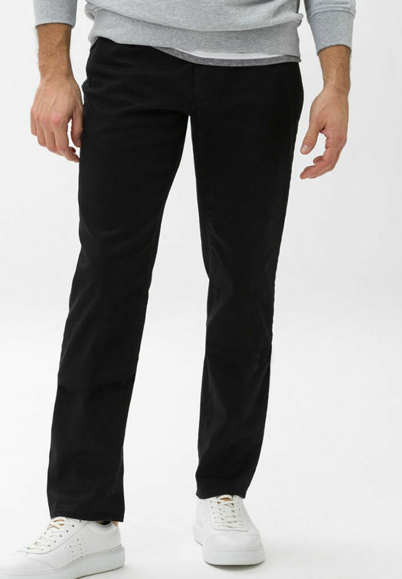 Schwarze Baumwollhose mit geradem Bein, die eine glatte Textur aufweist und mit weißen Sneakers getragen wird. Keine sichtbaren Muster oder Verzierungen.