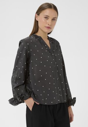 Blusa nera a pois realizzata in tessuto leggero, con maniche lunghe e polsini a volant e una chiusura frontale.