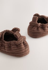 Chaussons en tissu marron avec un design texturé à côtes, doté d'un bord froncé et d'une ouverture souple et flexible pour un enfilage facile.