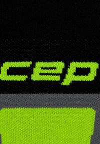Calze compressive nere con il brillante logo "CEP" verde. Presentano un motivo a maglia testurizzato e una fascia grigia, progettate per un uso atletico.