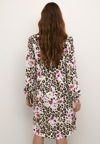Långärmad klänning med en beige bas som har leopardmönster och blommönster i rosa, vitt och mörkrött. Slätt tyg, avslappnad passform.