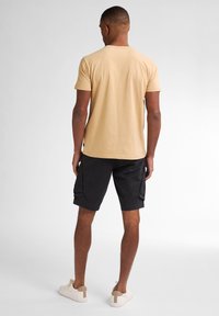 Tan bomulds t-shirt med korte ærmer, parret med sorte cargo shorts med sidelommer, og beige sneakers med en kontrasterende hælkant.