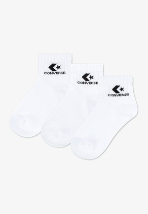Trois socquettes blanches avec le logo Converse noir et du texte sur le bord, disposées côte à côte sur un fond blanc.