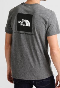 Šedé bavlněné tričko s kulatým výstřihem. Na zadní straně se nachází černý čtvercový grafický motiv s logem a sloganem "THE NORTH FACE". Krátké rukávy.