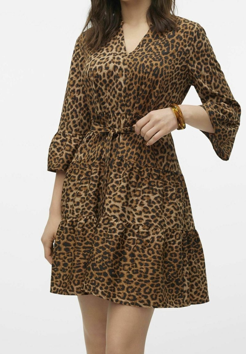 Robe à imprimé léopard avec un décolleté en V, des manches trois-quarts et une bordure à volants. Le tissu semble doux avec un léger éclat.