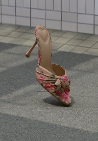Zapato de tacón alto con estampado floral y punta puntiaguda, sobre un fondo desnudo, con un detalle fruncido en la parte delantera y un acento de rosa.