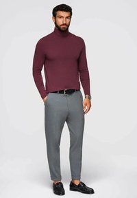 Mörkröd polotröja i kombination med ljusgrå skräddarsydda byxor och svarta fin skor. Elegant design med en figurnära silhuett och slät textur.