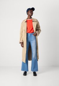 Beige trench coat, rød genser, lyseblå blussede jeans, svarte sko og marineblå caps. Jakken har en dobbeltspent design og rullede ermer.