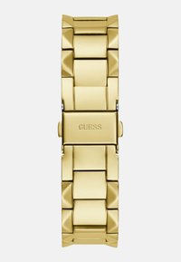 Pulsera de reloj de metal dorado con eslabones gruesos, con un acabado pulido y un cierre con el nombre de la marca embellecido.