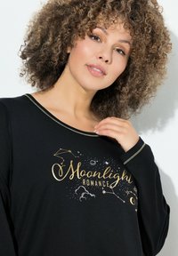 Černý top s dlouhými rukávy, zdobený zlatým nápisem "Měsíční romantika" a grafikou souhvězdí a mraků. Měkká tkanina, volný střih.