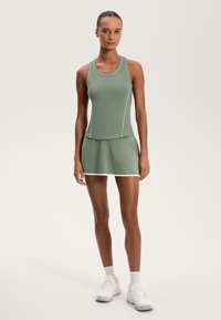 Aktív egészségügyi szett, amely egy zöld ujjatlan felsőből és egy passzoló szoknyás shortból áll. Texturált anyag, testhezálló dizájn, sportolási tevékenységekre alkalmas.