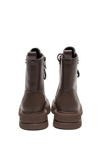 Botas de cuero marrón hasta el tobillo con una suela texturizada, paneles elásticos a los lados y una cremallera trasera para ponerlas y quitarlas fácilmente. Acabado liso con costuras mínimas.