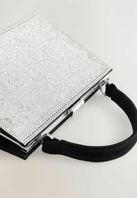 Silberne Clutch-Tasche mit strukturiertem Strass-Außenteil, schwarzem Wildleder-Tragegurt und metallischen Beschlägen. Quadratische Form mit einem Clipverschluss.